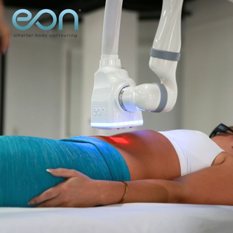 EON treatment head positioned over an abdomen, with turquoise trousers and a white top.